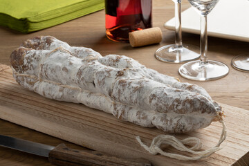 Whole French handmade dry sausage, Saucisson sec,  on a wooden cutting board 
