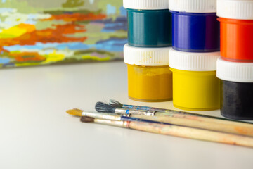 Jars of multi-colored gouache and brushes on a watercolor canvas background. Paints and brushes for...