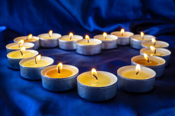 Lighted round candles are laid out in the shape of a heart on a dark blue background. A symbol of love, hope, warmth. Burning candles in the shape of a heart on a dark background.