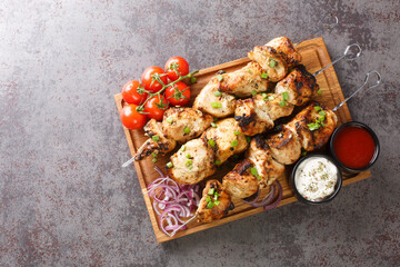 Juicy grilled chicken skewers with fresh vegetables and two sauces close-up on a wooden tray on a...