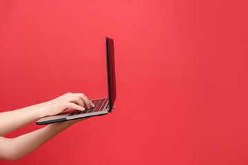 Close up of female hand holding working on laptop pc computer typing on keyboard, isolated over red...