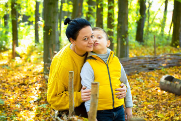 Happy portrait of mother and son hugging in autumn park.
