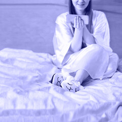 Toned with Very Peri young woman wearing llama slippers and gown in bed with smart phone. Square concept for Social media addiction with copy space for text. Depressive violet color mood.