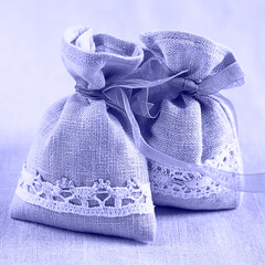Toned with Very Peri color Two linen sacks filled with dried lavender decorated with lacework and violet ribbon coque, aroma sachet. Closeup composition on the natural flaxen background. Square