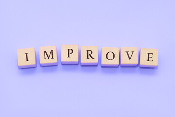 The word IMPROVE is made of wooden cubes on a violet background.
