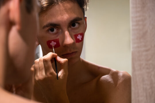 Swiss football fan preparing for serious match with painted face. Passion for football.