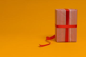 gift box wrapped in wrapping paper with red ribbon on yellow background, copy space
