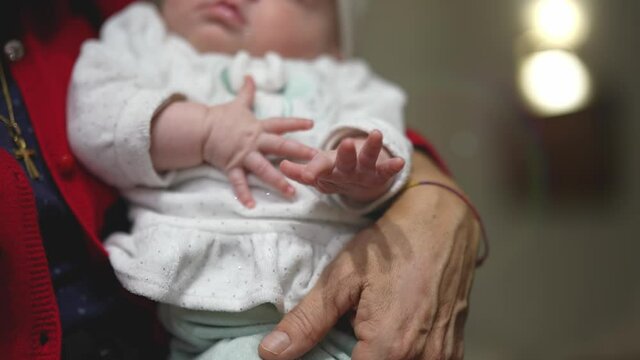 Closeup on little hands of an infant girl in her mother's or granma's arms.