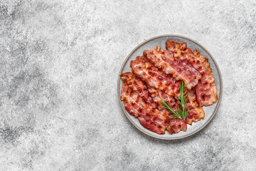 Fried bacon in a plate on a gray grunge background. Top view, flat lay
