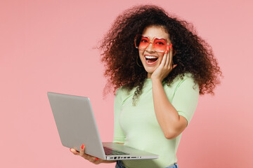 Vivid overjoyed young curly latin woman 20s years old wear mint t-shirt sunglasses hold use work on...