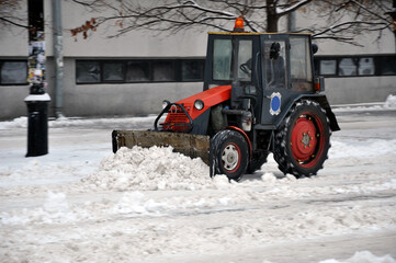 A snowblower removes snow in the city. A snow plow tractor shovels snow with a shovel.
