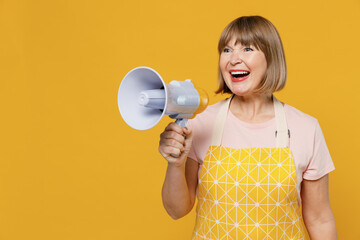 Elderly housekeeper housewife woman 50s in orange apron hold scream megaphone announces discounts...