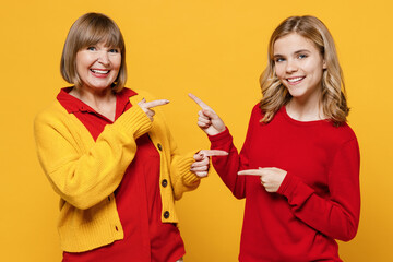 Happy fun woman 50s in red shirt have fun with teenager girl 12-13 years old. Grandmother granddaughter point index fingers on each other isolated on plain yellow background. Family lifestyle concept.