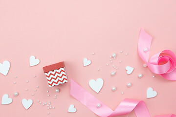 Composition with gift box, pink ribbons, white hearts and pearls on a pink background.