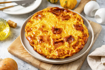 Frittata with pumpkin, bacon and ricotta in a ceramic plate on a light culinary background. Traditional Italian delicious homemade egg dish on the kitchen table closeup	