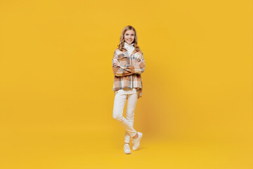 Fototapeta na wymiar Full body smiling happy confident little blonde caucasian kid girl 13-14 years wearing checkered shirt hold hands crossed folded isolated on plain yellow background studio. People lifestyle concept.