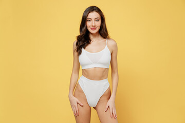 Fototapeta na wymiar Smiling skinny sexy lovely attractive young brunette woman 20s in white underwear with beautiful perfect fit body standing posing looking camera isolated on plain yellow background studio portrait