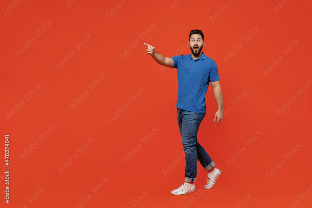 Canvas Prints Full body young smiling happy european caucasian man 20s wear basic blue t-shirt walking going point index finger aside isolated on plain orange background studio portrait. People lifestyle concept.