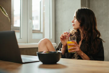 The portrait of beautiful young woman working with laptop while breakfast with strawberries and drinking orange juice. Eating at home.