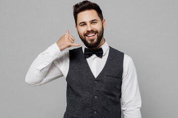 Young fun barista male waiter butler man 20s in white shirt vest elegant uniform work at cafe doing phone gesture like says call me back isolated on plain grey background Restaurant employee concept