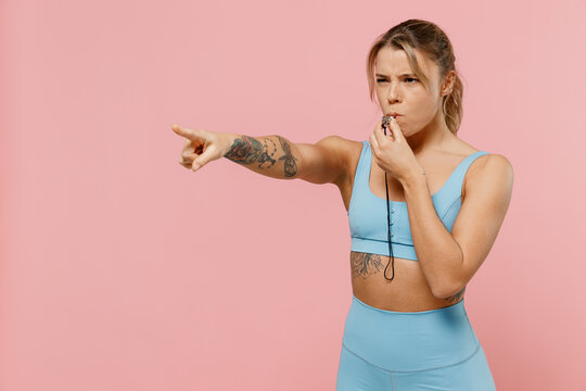 Young strong sporty athletic fitness trainer instructor woman wear blue tracksuit spend time in home gym whistle point finger aside isolated on plain pink background. Workout sport motivation concept.