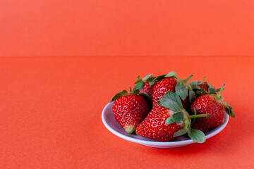 ripe strawberries on a plate on a red background, copy space