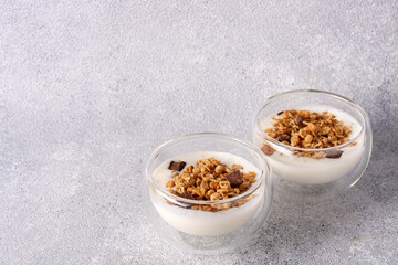 two glass cups with muesli, yogurt, chocolate on a gray background