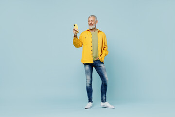 Full body elderly gray-haired mustache bearded man 50s wear yellow shirt hold in hand use mobile...