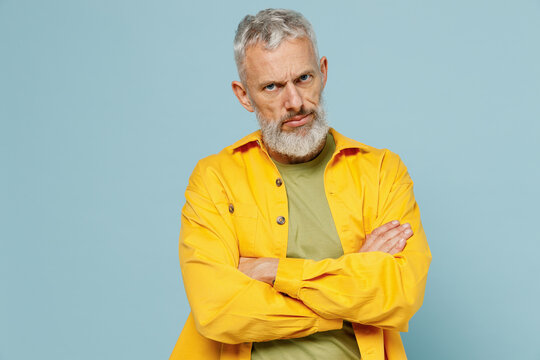 Elderly sad offended indignant shrewd gray-haired mustache bearded man 50s wear yellow shirt hold hands crossed folded isolated on plain pastel light blue background studio. People lifestyle concept.