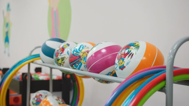 Colorful balls and hula hoops on rack near white wall in spacious hallway for children gymnastic training closeup