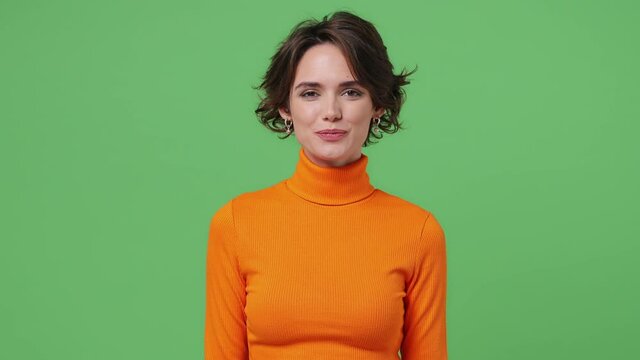 Smiling charming delight fun fascinating young brunette woman 20s wears orange shirt looking camera wink eye blink isolated on plain green background studio portrait. People emotions lifestyle concept