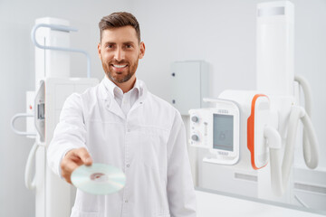 Handsome radiologist with beard given showing at camera silver CD plate with result after...