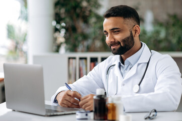 Focused Indian physician therapist conducts online consultation, communicates with his patient via video call using laptop, prescribes treatment, answers questions, gives recommendations