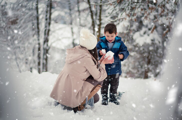 Young, beautiful mom and her little boy playing in the snow, making snowball