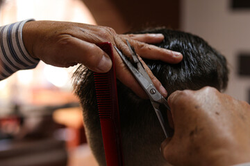Obraz na płótnie Canvas Barber hands with scissors cutting man's hair