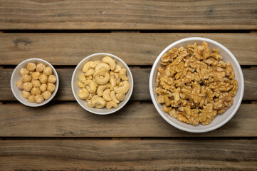 Hazelnuts, cashew nuts and walnuts in different jars on a wooden table in a top view and in a dark environment.