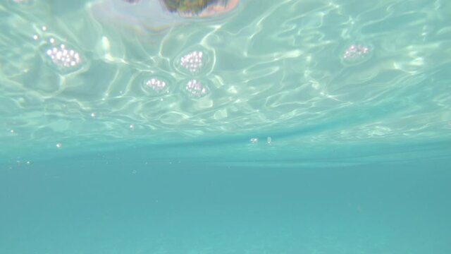 View on the sea shore from water. Underwater camera, swimming in ocean, sea. POV view from person who swim near the beach. Clean blue water and coast with trees and rocks. Someone sinking concept