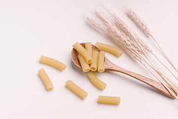 Dry pasta in wooden spoon and ears of wheat on light background. Elbow macaroni