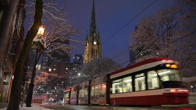 Streetcars pass by church during a winter snowfall in the city.
