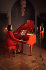 The girl plays the red piano. She is wearing a stylish and trendy red suit. Evening, candles.