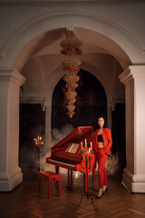 Fototapeta premium The girl plays the red piano. She is wearing a stylish and trendy red suit. Evening, candles.