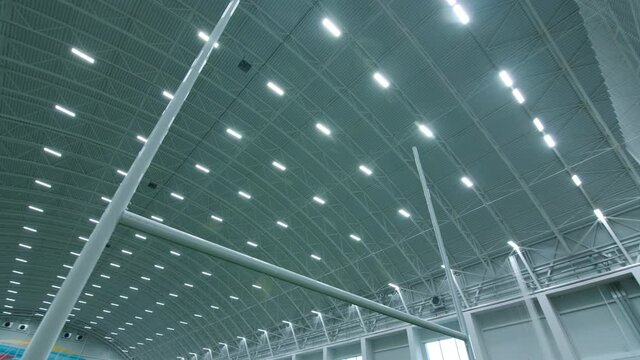 Large spacious hall of modern sports stadium with equipment and glowing led lights on arch ceiling low angle shot