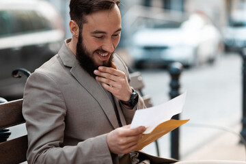 Happy businessman in a suit reads mail outside. Good results, pleasant surprise.