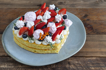 Heart-shaped cake decorated with red fruits and meringue. Wooden background. Valentine's Day. Copy space.