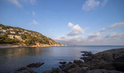Seascape. Mediterranean evening. Rocks surrounded by water on the beach protruding into the sea on a sunny day, Blanes, Catalonia, Spain.