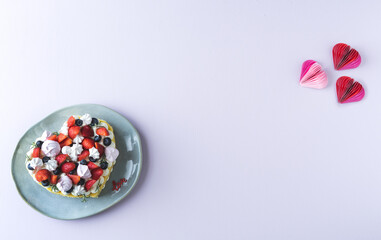 Heart-shaped cake decorated with red fruits and meringue. White background. Valentine's Day. Copy space.