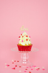 Valentine's Day. A cupcake with cream and red topping decoration with a wooden sign with the word LOVE on a pink background. Vertical photo.