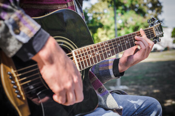 Fototapeta na wymiar Young man play solo guitar while sitting on park bench