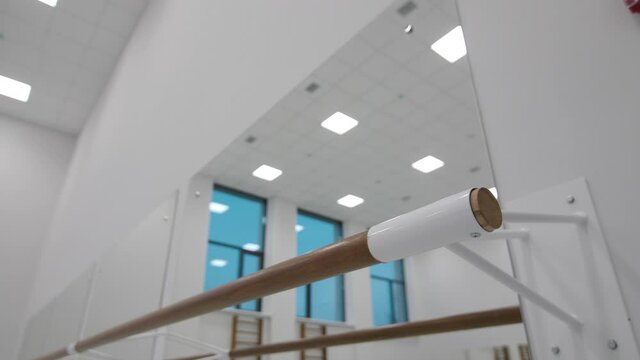 Wooden bar near large mirror on wall in brightly lit dance class in contemporary sports complex extreme close view
