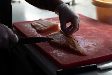 Photo of male hands in gloves which cuts a red fish on a board. Seafood and food